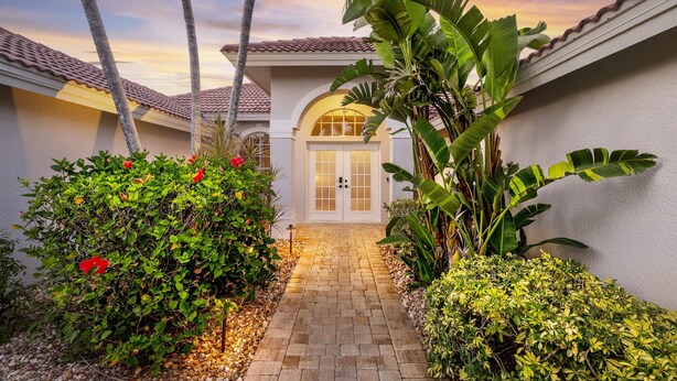 Un sendero lleva a una casa con techo de tejas, rodeada de abundante vegetación y palmeras.