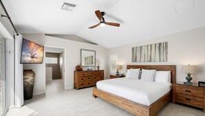 Un dormitorio con una cama de madera, un ventilador de techo, un cuadro grande y vistas al exterior.