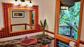 A bathroom with a red-tiled wall, a marble sink, a mirror, and a view of a tropical garden through a window. - VERY PRIVATE, expansive ocean VIEWS, close to BEST BEACH (Kailua-Kona)