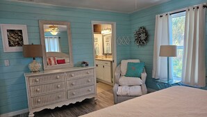 A bedroom with a bed, a dresser, a chair, a mirror, and a window with curtains. - Newly Renovated Island Pool Home
 (Captiva)