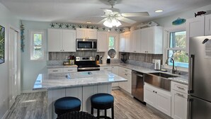 A modern kitchen with white cabinets, stainless steel appliances, a central island with stools, and a ceiling fan. - Newly Renovated Island Pool Home
 (Captiva)