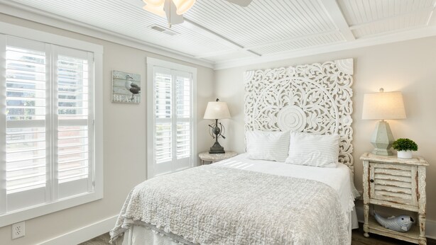 Une chambre à coucher avec un grand lit, deux tables de chevet, un ventilateur de plafond et une tête de lit décorative.