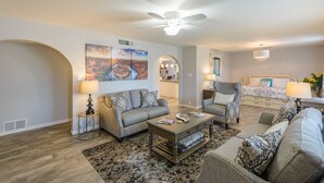 A spacious living room with a large sofa, a coffee table, and a patterned rug. There is a ceiling fan and a chandelier. - Scottsdale 4BR – Heated Pool, Putting Green, 5 Min to Old Town (Scottsdale)