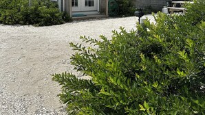 A two-story house with a gravel driveway, a covered porch, and a small garden area with shrubs and flowers. - Cottage is on a PRIVATE BEACH shared between two houses.  (East Sandwich)