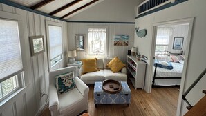 A cozy room with a white sofa, a small table, and a bed with a blue and white patterned bedspread. - Cottage is on a PRIVATE BEACH shared between two houses.  (East Sandwich)
