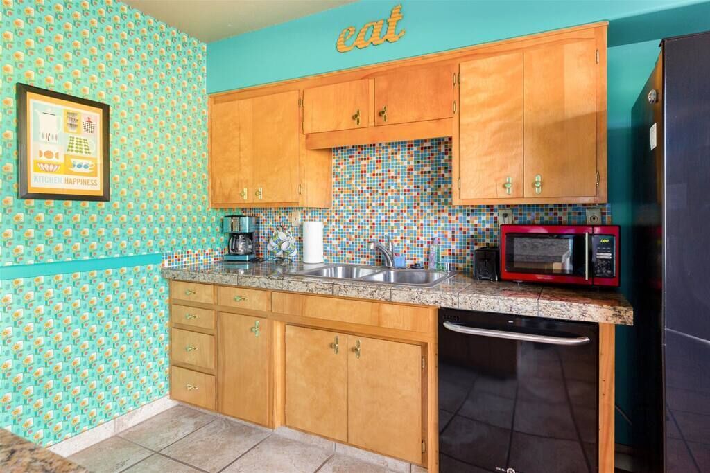 A kitchen with wooden cabinets, a tiled backsplash, a sink, a microwave, and a dishwasher.