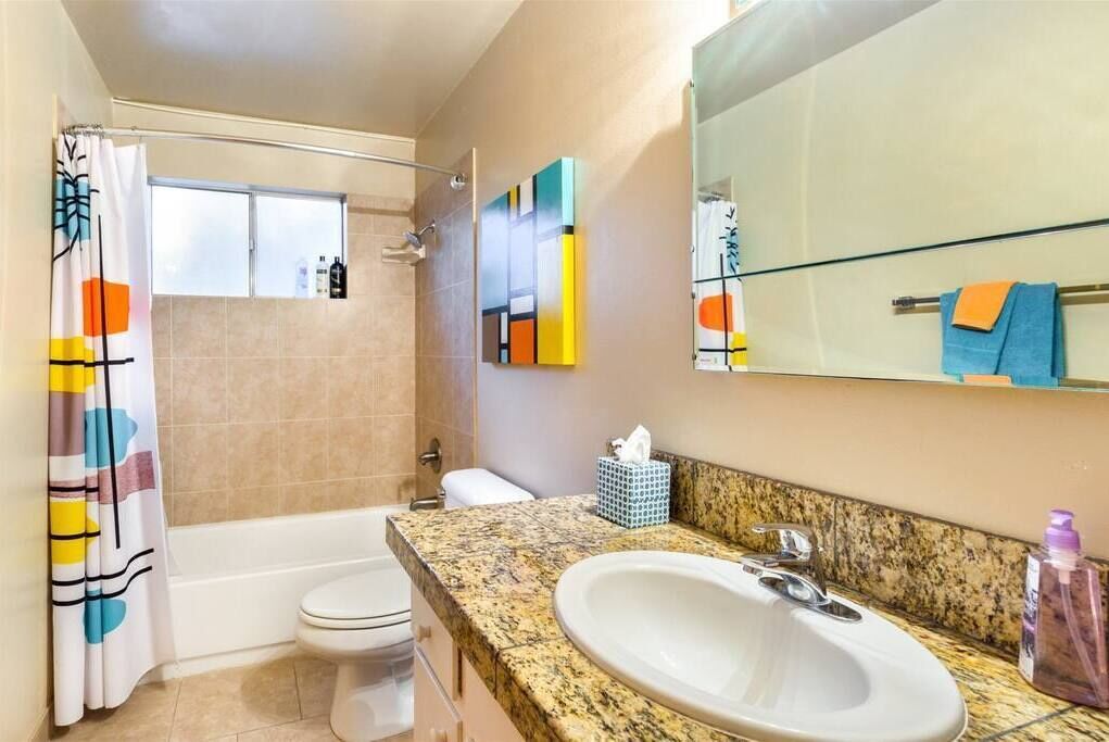 A bathroom with a bathtub, toilet, and sink. There is a shower curtain with a colorful design, a towel rack with a blue towel, and a mirror above the sink.