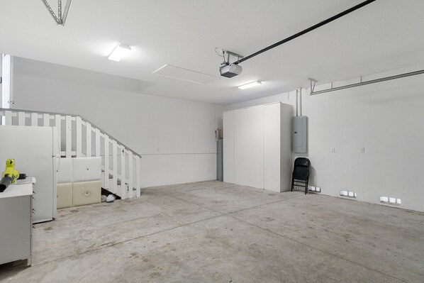 Un garage spacieux et bien éclairé, doté d’un sol en béton, de murs blancs et d’un escalier blanc.