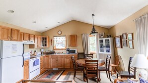A kitchen with wooden cabinets, a refrigerator, stove, microwave, and a dining area with a table and chairs. - Private And Secluded Rental On the Kalamazoo River - Saugatuck-Douglas-Fennville (Fennville)