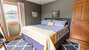 A bedroom with a bed, a window with curtains, a ceiling fan, and two wall-mounted pictures. - Private And Secluded Rental On the Kalamazoo River - Saugatuck-Douglas-Fennville (Fennville)