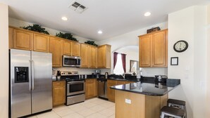 A modern kitchen with wooden cabinets, stainless steel appliances, a central island, and bar stools. - 🏰 Magical 6-Bed Family Villa ✨[FREE Heated Pool, Spa & BBQ] 5 Mins to Disney 🎢 (Kissimmee)