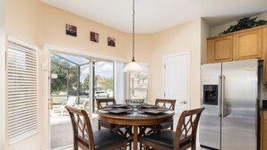 A kitchen with a stainless steel refrigerator, wooden cabinets, and a dining area with a round table and chairs. - 🏰 Magical 6-Bed Family Villa ✨[FREE Heated Pool, Spa & BBQ] 5 Mins to Disney 🎢 (Kissimmee)
