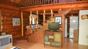 Een rustiek houten interieur met een wenteltrap, een televisie op een kast en een koelkast.
