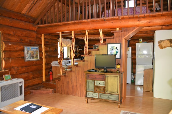 L’intérieur d’un chalet rustique, avec un escalier en bois, un téléviseur posé sur un meuble et un réfrigérateur.