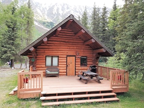 Une cabane en rondins avec une terrasse en bois, une table de pique-nique et un banc.