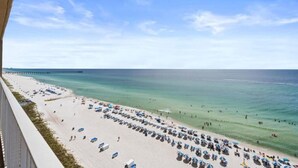 Blick auf einen Strand mit einem Pier in der Ferne, angebundenen Strandsonnenschirmen und einem klaren Himmel.