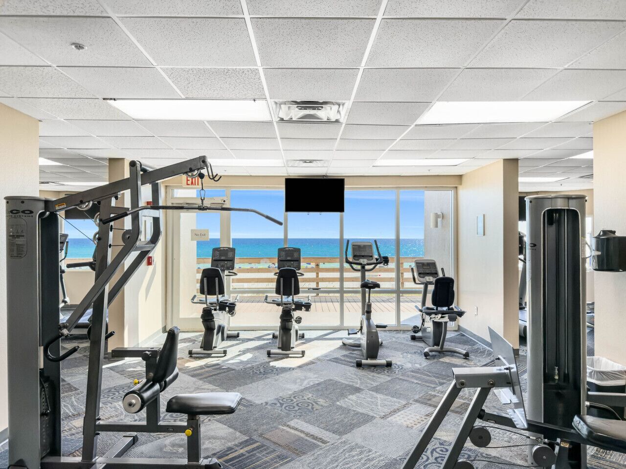 A gym with cardio machines, weight equipment, and a view of the beach.