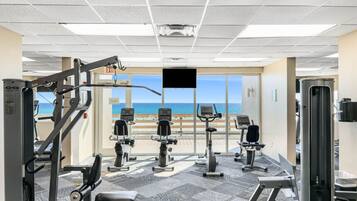 A gym with cardio machines, weight equipment, and a view of the beach.