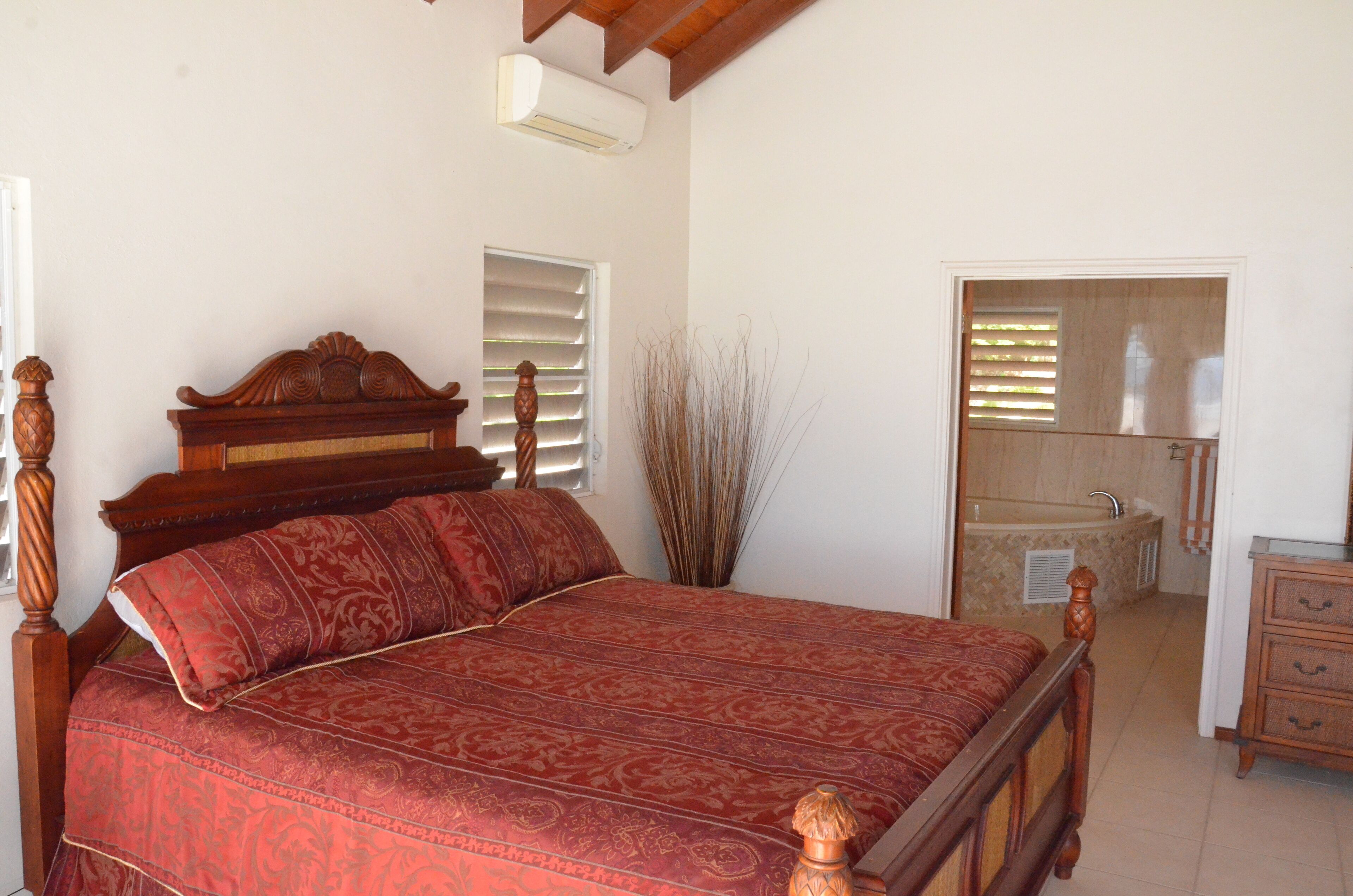A bedroom with a wooden bed, a bathroom with a bathtub, and a wooden dresser.
