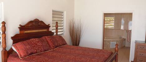 A bedroom with a wooden bed, a bathroom with a bathtub, and a wooden dresser.