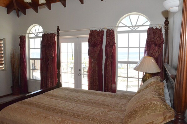 A bedroom with a large bed, two windows with curtains, a lamp, and a view of the outdoors.