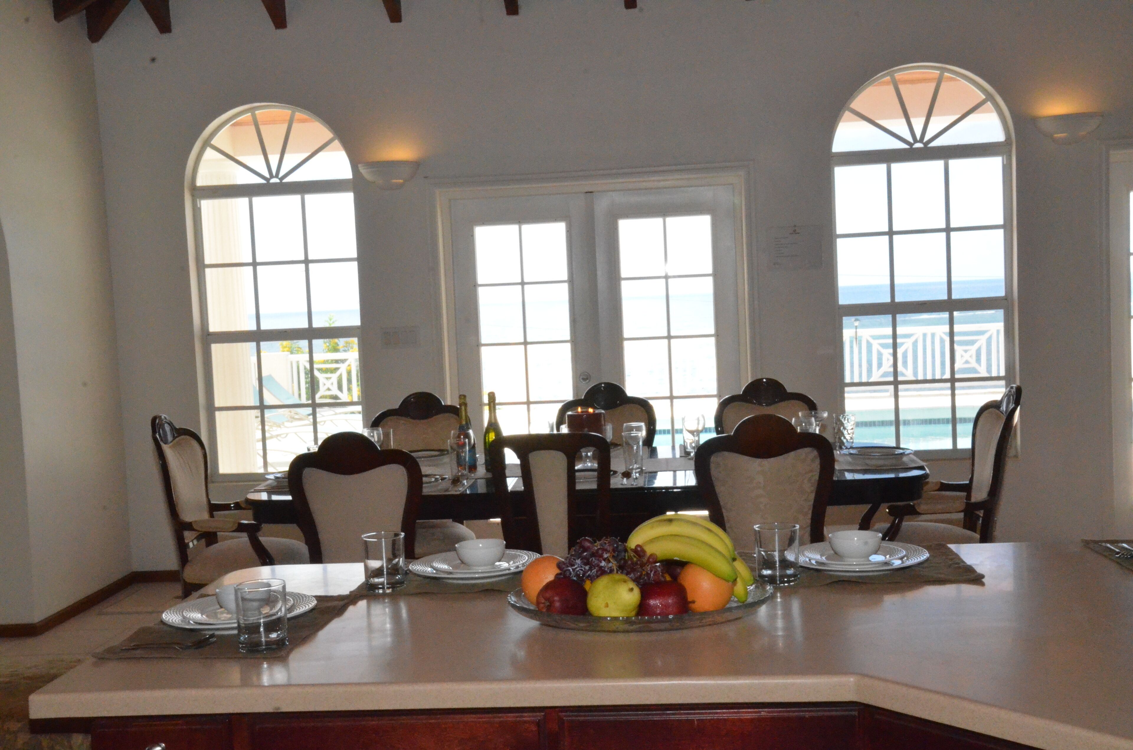 A dining area with a table set for four, featuring a fruit platter, white plates, and glasses.