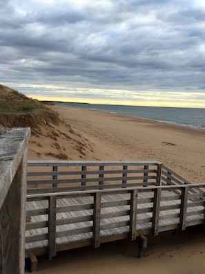 Un paseo marítimo de madera que conduce a una playa arenosa, con dunas al fondo.