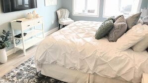 A bedroom with a bed, a TV mounted on the wall, a chair, and a window.