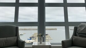 A room with large windows overlooking a marina, featuring two armchairs and a small table with a vase.