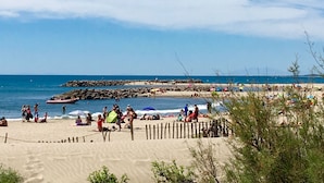 Une plage où l’on peut se détendre au soleil et se baigner, une digue rocheuse et un ciel dégagé.