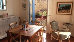Un coin repas avec une table et des chaises en bois, une petite table ronde avec une chaise, une lampe fixée au mur et un tableau encadré.