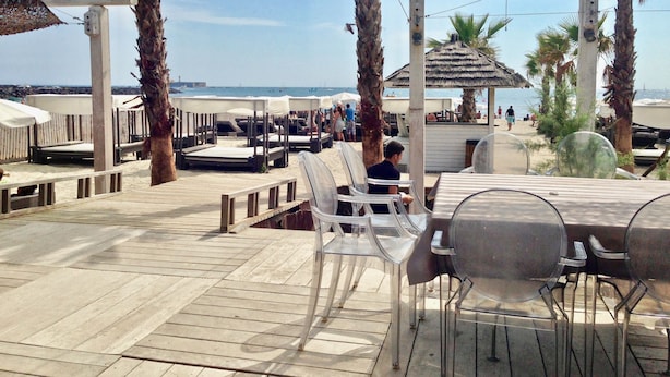 Un restaurant situé en bord de mer, avec une terrasse, des palmiers et une vue sur l’océan.