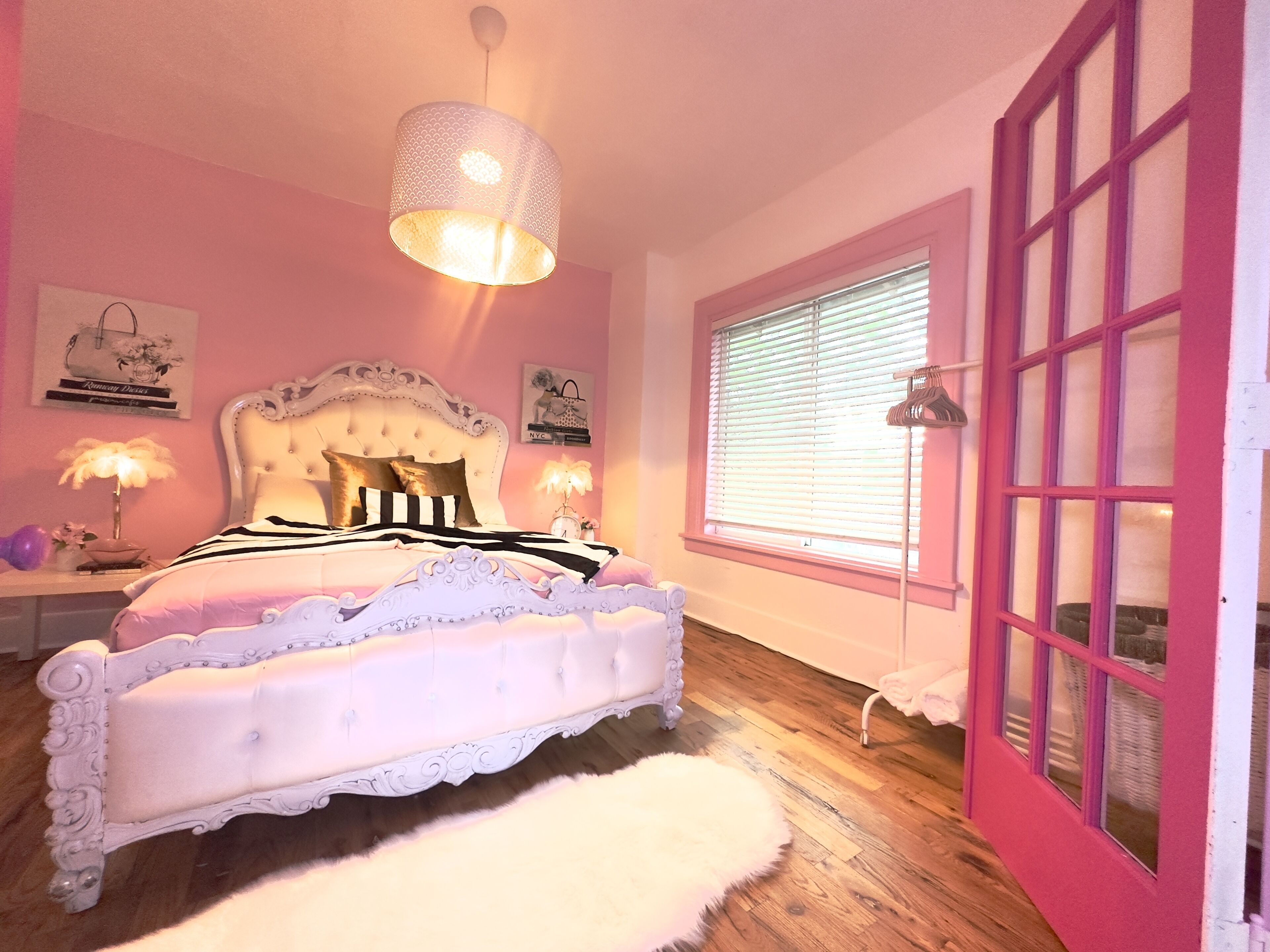 A pink-themed bedroom with a white ornate bed, a fluffy white rug, and a window with blinds.