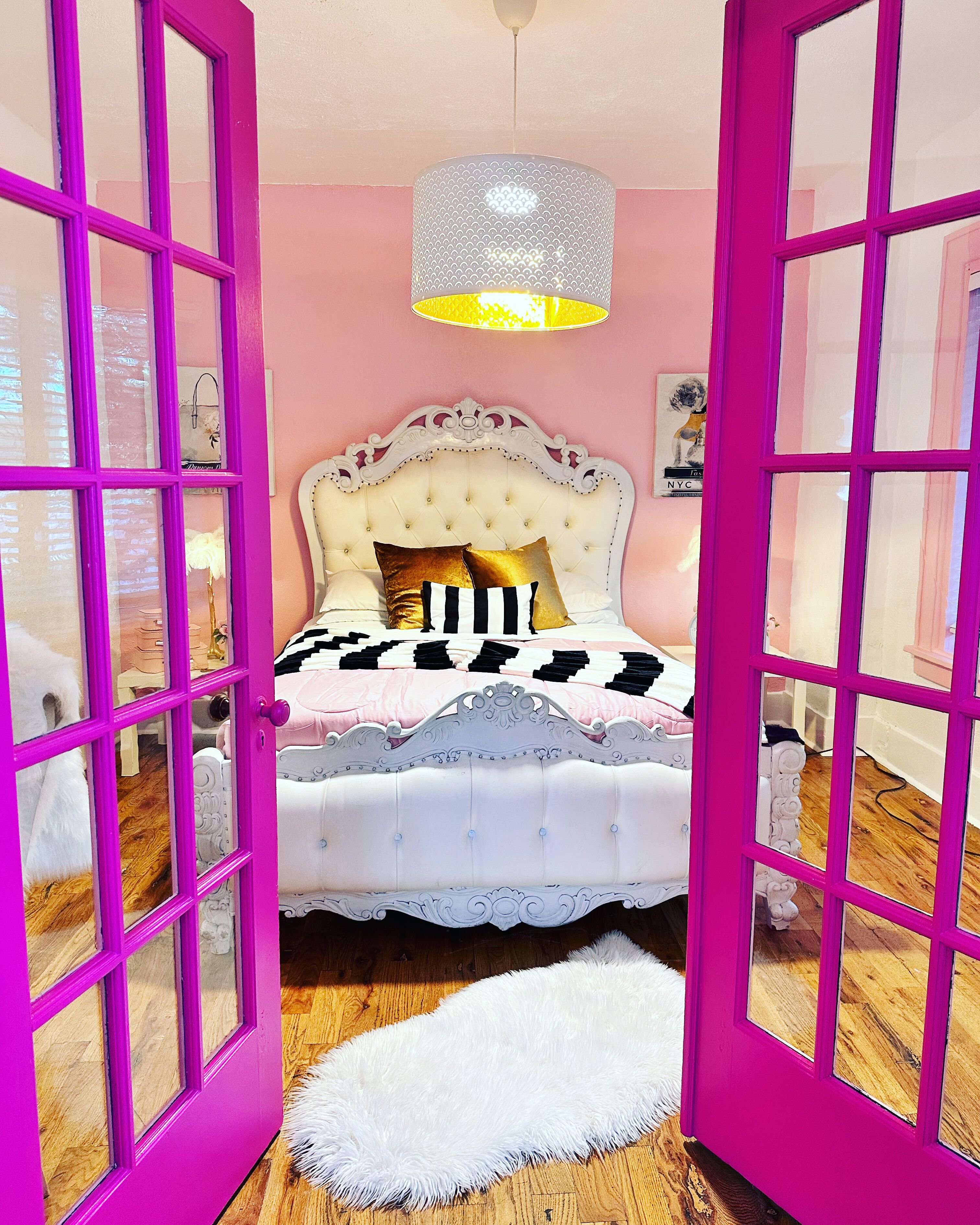 Une chambre avec une tête de lit blanche à motifs capitonnés, un chambranle de porte rose et un tapis blanc à poils longs.
