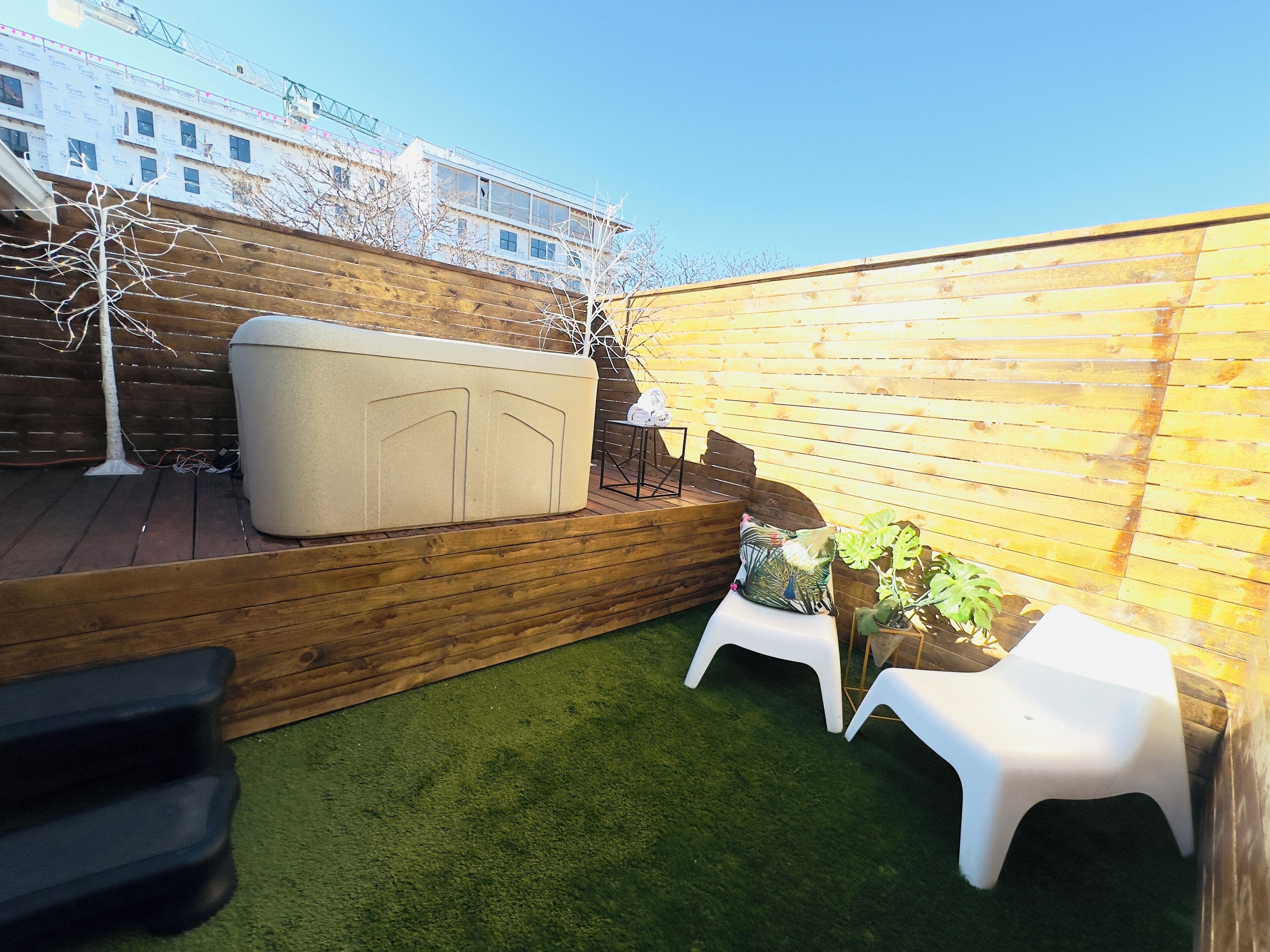 A small backyard with a wooden deck, a white outdoor sofa, and a small table with chairs.