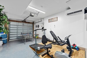 Ein Heimfitnessraum mit Trainingsgeräten, einem Tischtennis-Tisch und einer Garagentür.