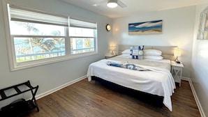 A bedroom with a bed, a ceiling fan, a window with blinds, a nightstand, and a bench. - Twin Beaches: 2 houses ON the ocean/ON the river +Private Docks,Hot Tubs & More! (Stuart)