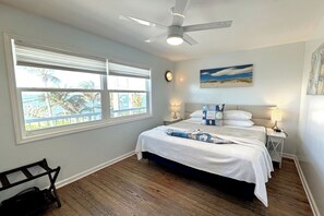 A bedroom with a bed, a ceiling fan, a window with blinds, a nightstand, and a bench.