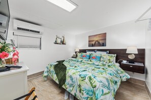 A bedroom with a bed, nightstands, a painting, and a desk with a lamp.