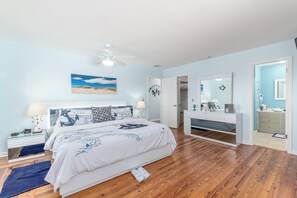 Un dormitorio con cama, mesitas de noche, cómoda, ventilador de techo y un espejo grande.