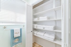 A bathroom with a white towel rack, a towel with a seashell and starfish design, and a white towel shelf.