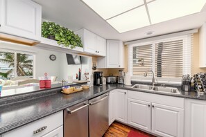 A modern kitchen with white cabinetry, a stainless steel sink, and a window with blinds.