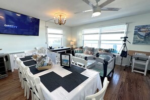 A dining area with a large flat-screen TV displaying DIRECTV, a chandelier, and a ceiling fan. - Twin Beaches: 2 houses ON the ocean/ON the river +Private Docks,Hot Tubs & More! (Stuart)