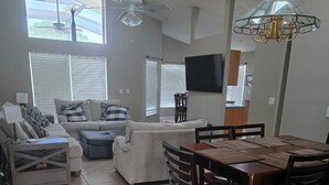 A spacious living room with a sofa, a dining table with chairs, a ceiling fan, and a TV mounted on the wall. - Pet-Friendly Fenced Home w/Pool & Spa Heat - 3 Miles from Disney (Kissimmee)