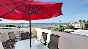 A terrace with a table and chairs, a red umbrella, and a view of the sea and buildings. - Enjoyable and Luxurious Carlsbad Village Beach House 1/2 Block to Beach (Carlsbad)