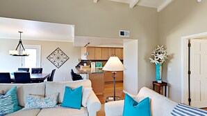 A living room with two white sofas, a dining area with a table and chairs, a kitchen with wooden cabinets, and a hallway with a door. - Enjoyable and Luxurious Carlsbad Village Beach House 1/2 Block to Beach (Carlsbad)