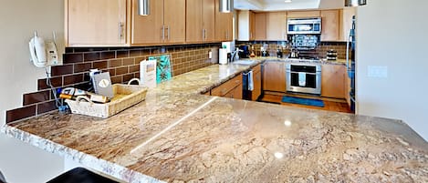 Eine moderne Küche mit Granitabdeckungen, Holzschränken und Edelstahlgeräten.