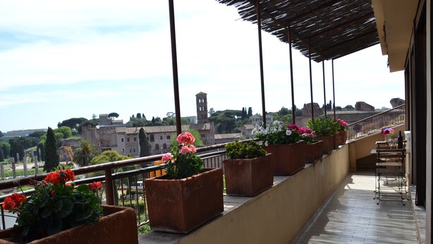 Varanda com plantas em vasos e vista para uma cidade histórica.