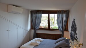Quarto com cama, guarda-roupa, janela com cortinas e um objeto decorativo na parede.
