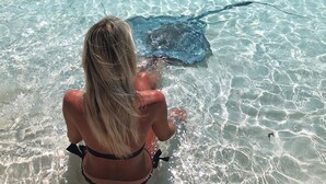A woman sitting in shallow water observing a stingray. - LARGE 4 Bed/4Bath BEACHFRONT APARTMENT SLEEPS 8 and directly  on HOOPERS BAY (Georgetown)